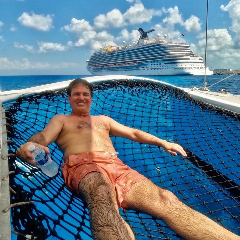 Traveler relaxing on a catamaran net in front of a cruise ship in Cozumel